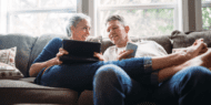 Photo of a man and woman sitting on a couch looking at a tablet